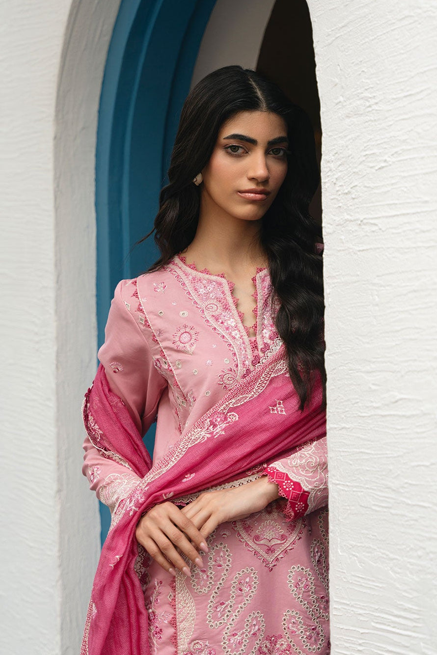 Woman in a pink embroidered outfit standing in a white archway.